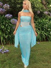 Woman in a light blue dress standing outdoors with greenery and flowers in the background
